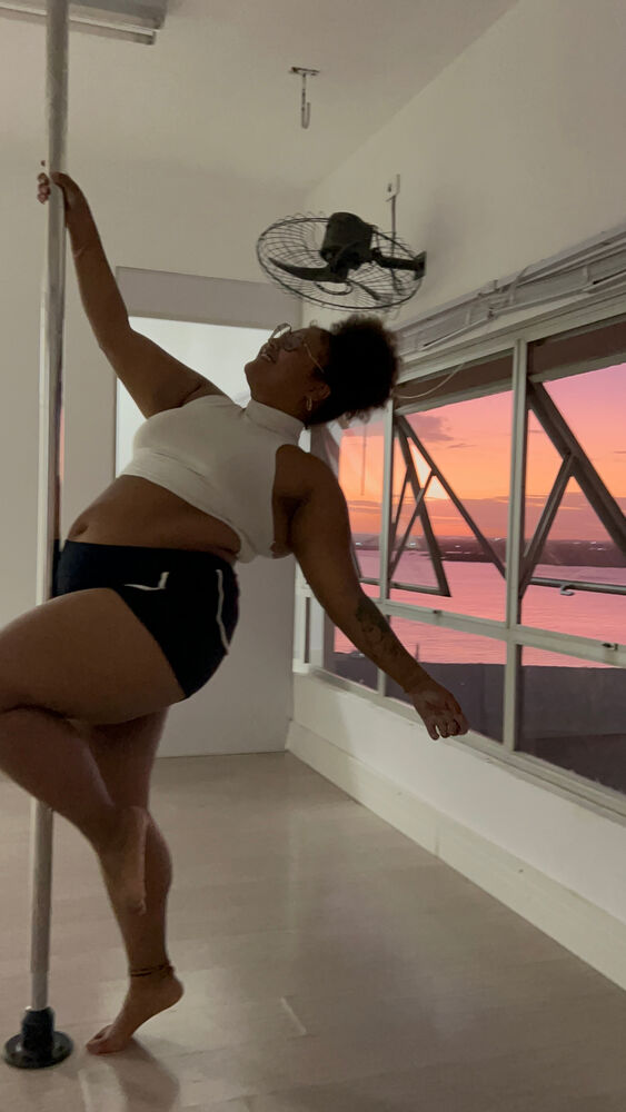 Aluna treinando na barra de pole ao lado da janela, ao pôr do sol