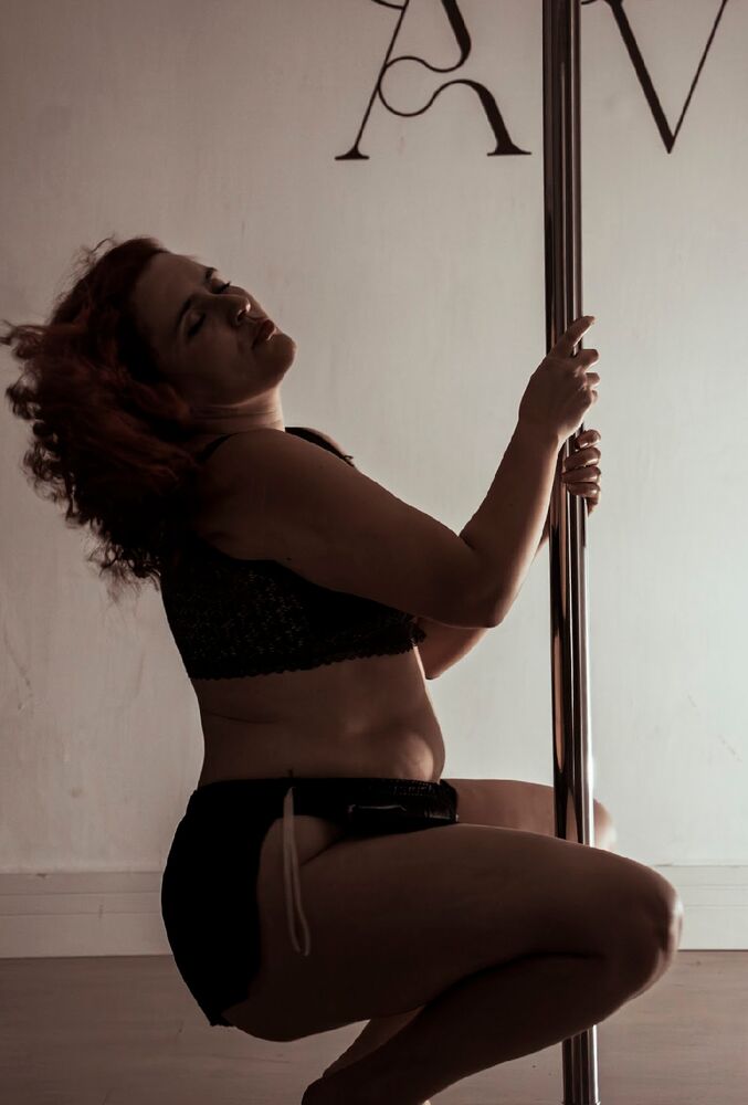 Aluna agachada segurando a barra de pole